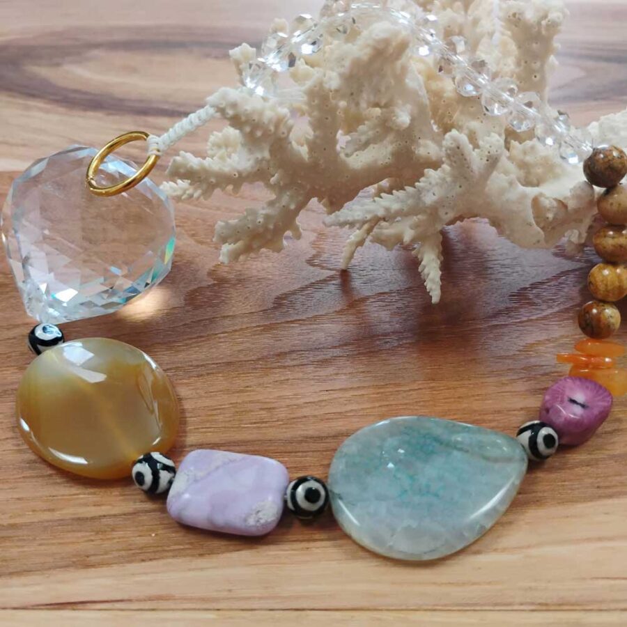 Handmade crystal suncatcher featuring a Three-Eye Dzi agate bead at the center, accented with purple amethyst beads, dyed agate beads, and clear faceted crystal elements, arranged in a circular design on a light background.