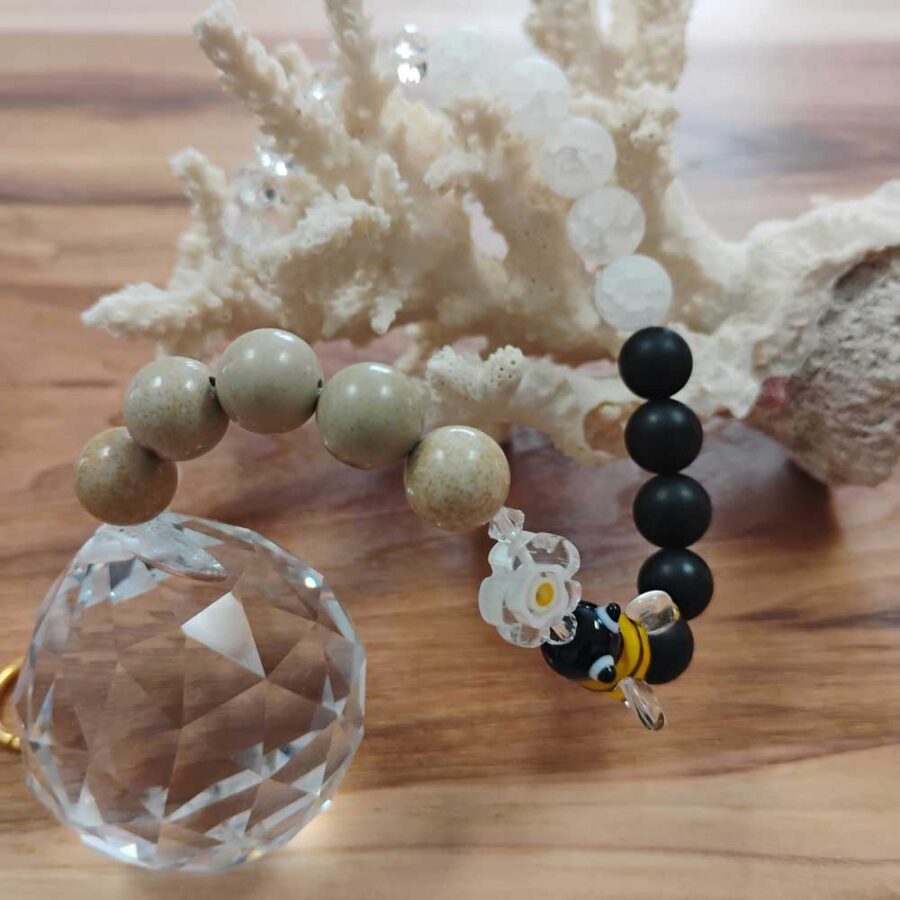 Handmade crystal suncatcher with a faceted clear glass crystal, white and black gemstone beads, picture jasper stones, and a small glass bee bead, arranged in a circular shape on a light background.